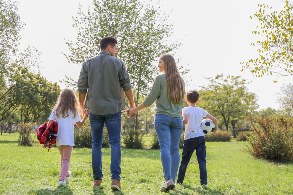 A family walking through a park with a soccer ball