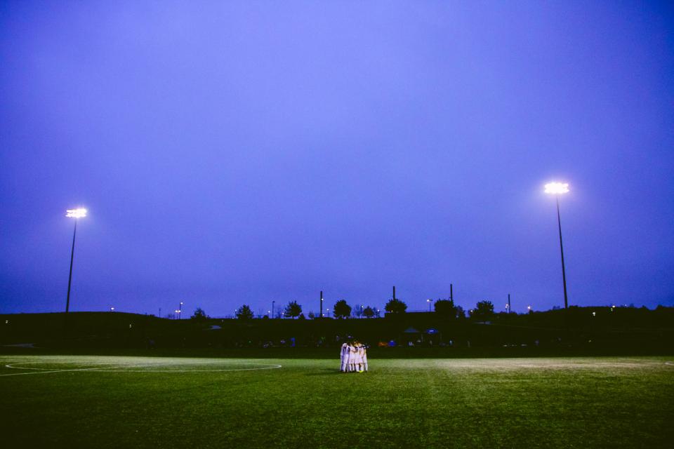Players gathering in a team huddle beneath field lights